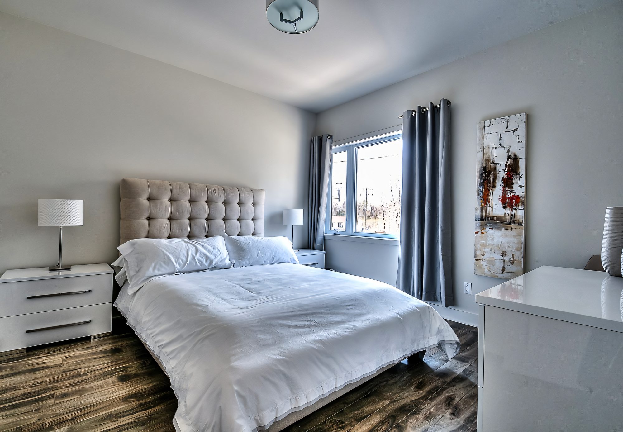 Chambre principale au Quartier Eaux-Vives : tête de lit capitonnée, plancher de bois, fenêtre sur la forêt