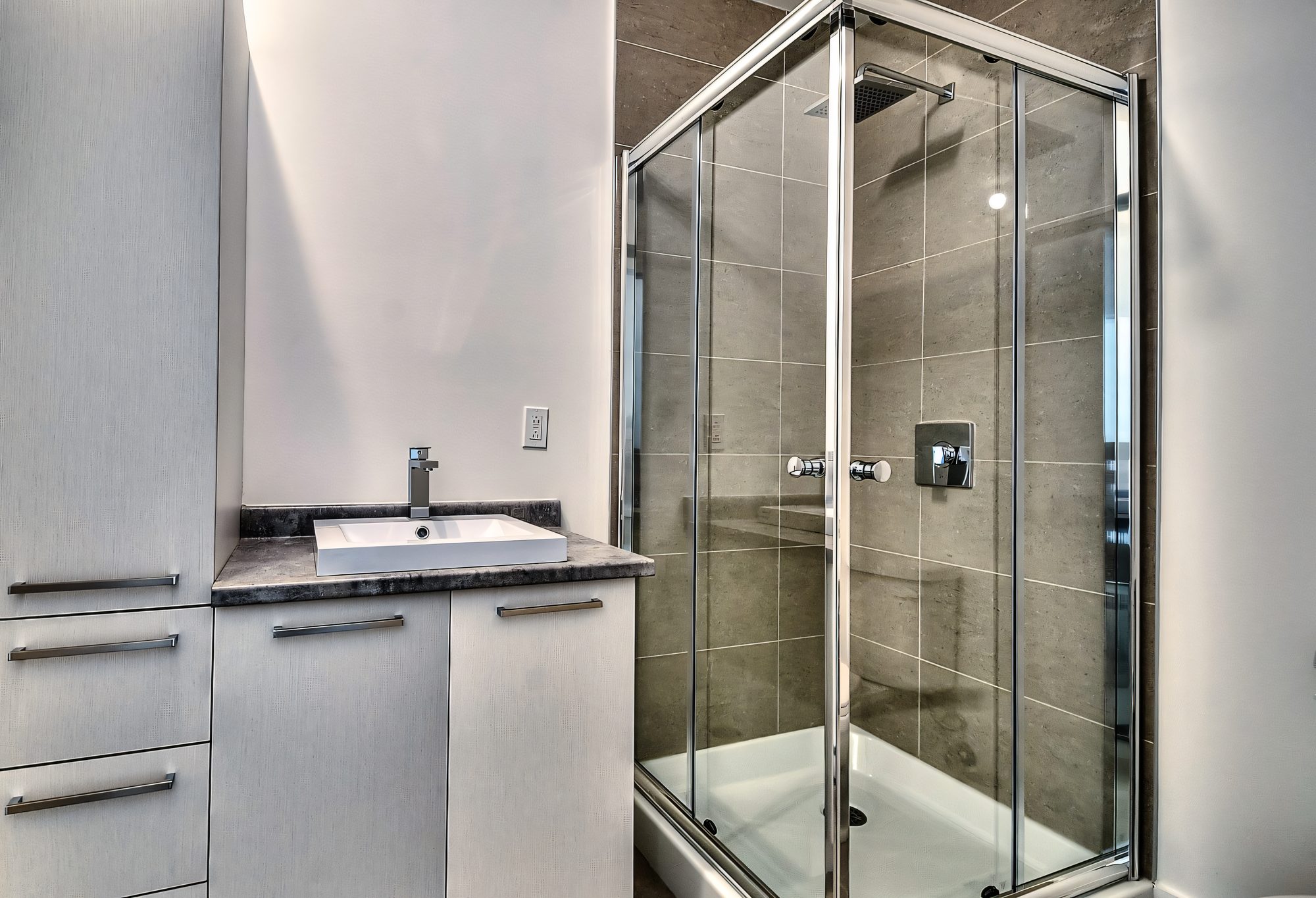Salle de bain au Quartier Eaux-Vives : douche vitrée, céramique grise, meuble-lavabo blanc